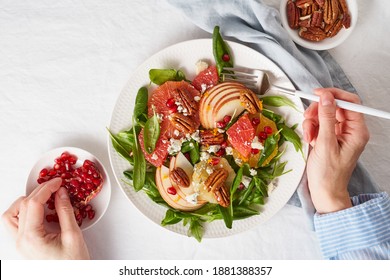 Eating Fruits Citrus Salad With Nuts, Green Lettuce. Balanced Food. Top View Of Woman Hands With Plate Of Meal Of Spinach With Orange, Grapefruit, Apples, Pecans