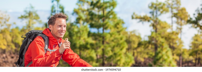 Eating Granola Bar Snack On Forest Hike Happy Camper Man Hiking In Nature Landscape Holding Healthy Food Breakfast Bar. Banner Panoramic