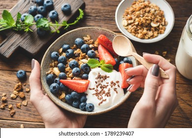 Eating Granola With Greek Yogurt And Berries. Female Hands Holding Bowl Of Healthy Breakfast Cereals Granola With Fruits And Yogurt. Concept Of Clean Eating, Dieting