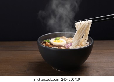 Eating hot vegetarian ramen with chopsticks at wooden table against black background. Space for text - Powered by Shutterstock