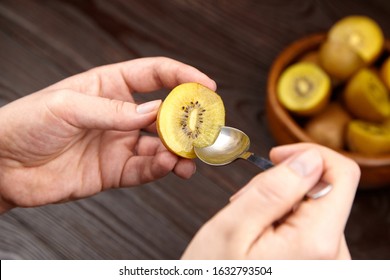 Eating Kiwi Gold Fruit. Hands With Spoon And Half Of Ripe Juicy Kiwi With Yellow Flesh On Wooden Background