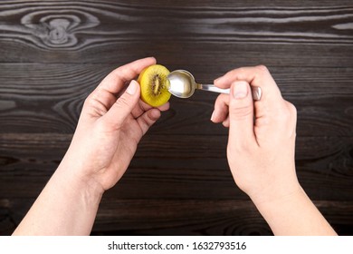 Eating Kiwi Gold Fruit. Hands With Spoon And Half Of Ripe Juicy Kiwi With Yellow Flesh On Wooden Background, Top View