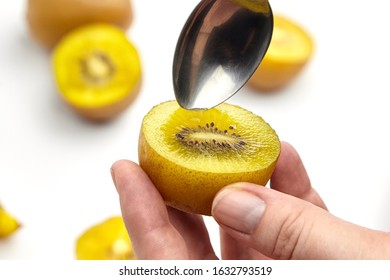 Eating Kiwi Gold Fruit. Hands With Spoon And Half Of Ripe Juicy Kiwi With Yellow Flesh On White Background