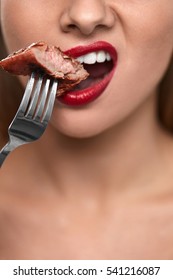 Eating Meat. Closeup Of Woman Mouth With Red Lips, White Teeth Biting Tasty Beef Steak On Fork. Close-up Of Beautiful Female Mouth Eating Delicious Grilled Meat. Nutrition Concept. High Resolution