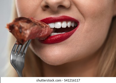 Eating Meat. Closeup Of Woman Mouth With Red Lips, White Teeth Biting Tasty Beef Steak On Fork. Close-up Of Beautiful Female Mouth Eating Delicious Grilled Meat. Nutrition Concept. High Resolution