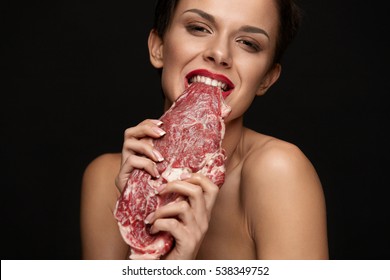 Eating Meat. Hungry Woman With Red Lips Going To Eat Raw Meat. Portrait Of Girl With Beautiful Face Makeup Biting Beef Steak Meat With Her Teeth. High Protein Diet And Food Concept. High Resolution