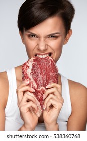 Eating Meat. Hungry Woman Ripping Raw Red Meat With Her Healthy White Teeth. Closeup Portrait Of Beautiful Girl Biting Beef Steak Meat With Greed. Hunger, Food And Nutrition Concept. High Resolution