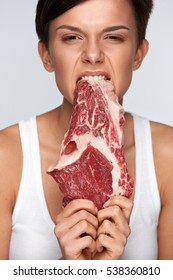Eating Meat. Hungry Woman Ripping Raw Red Meat With Her Healthy White Teeth. Closeup Portrait Of Beautiful Girl Biting Beef Steak Meat With Greed. Hunger, Food And Nutrition Concept. High Resolution