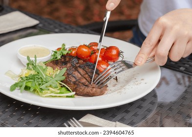 Eating meat with tomatos, arugula. Steak with garnish and sauce on a plate.
Man cuts ready juicy meat steak