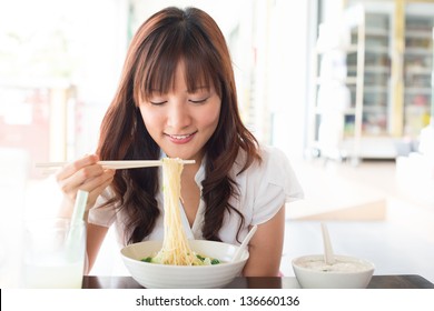 Eating Noodles At Restaurant. Young Asian Girl Eating Ramen Noodles Using Chopsticks.