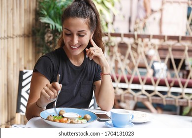 Eating out, lifestyle and travelling concept. Portrait of pretty european woman eating at restaurant table healthy food, drinking coffee, dining alone, smiling, tourist at cafe of her hotel