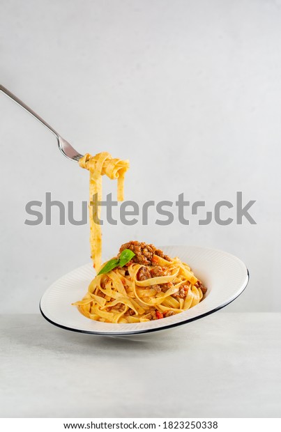 Eating pasta. Egg pasta tagliatelle with bolognese\
sauce made from meat and tomato sauce. Traditional italian dish\
from Bologna. Dynamic photo. Minimalism. Light grey background.\
Copy space.