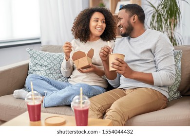 eating and people concept - happy african american couple with takeaway food and drinks at home