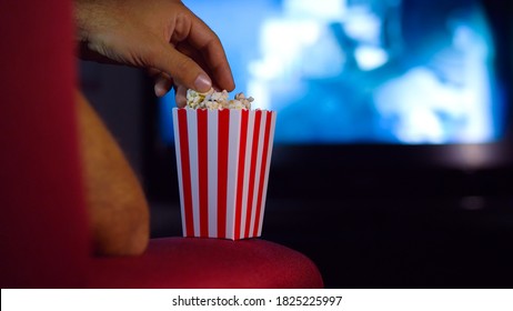 Eating popcorn while watching a movie on the couch at home. Scene in a house with bright lights, a movie night with the scent of pop corn.
