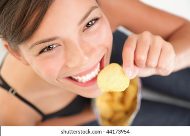 Eating Potato Chips / Crisps.  Cute Woman Having A Junk Food Snack While Looking Up At Camera. Adorable Mixed Race Chinese / Caucasian Model.