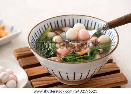 Eating red and white small tangyuan, tang yuan, glutinous rice dumpling balls with savory soup in a bowl on white table background.