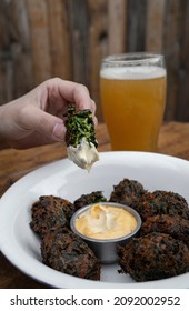 Eating In The Restaurant. Closeup View Of A Woman Dipping A Spinach Fritter In A Garlic Aioli Sauce. A Pint Of Beer In The Background. 