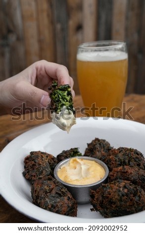 Eating in the restaurant. Closeup view of a woman dipping a spinach fritter in a garlic aioli sauce. A pint of beer in the background. 