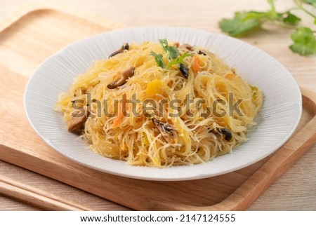 Eating rice vermicelli noodles stir-fried with boiled pumpkin and vegetables on wooden table background.