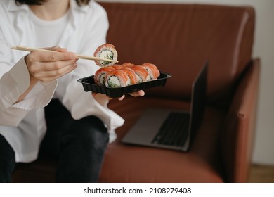 Eating sushi roll with chopsticks, sushi delivery package, tasty meal, tuna roll, laptop