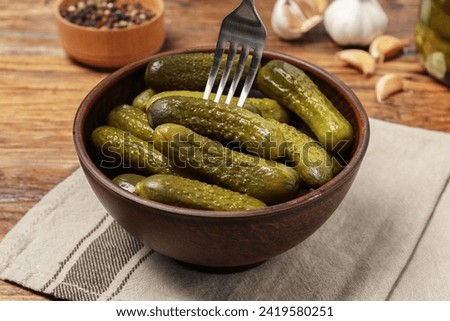 Eating tasty pickled cucumbers with fork at wooden table