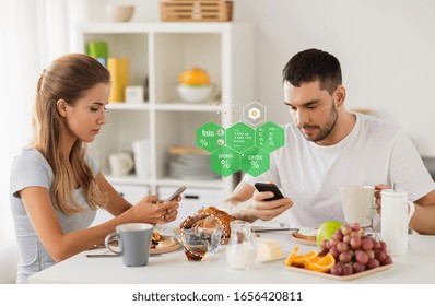 Eating, Technology And People Concept - Couple With Smartphones Having Breakfast At Home Over Food Nutritional Value Chart