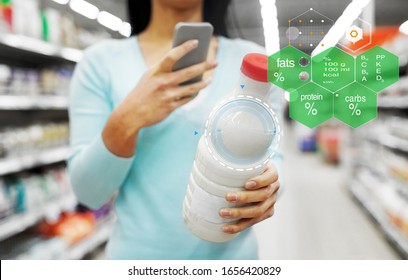 Eating, Technology And People Concept - Young Woman With Smartphone Holding Milk Bottle At Grocery Store Or Supermarket Over Food Nutritional Value Chart