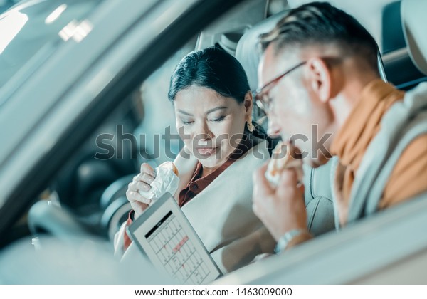 Eating together.\
Husband and wife looking at the laptop screen and eating sandwiches\
having lunch in the car.