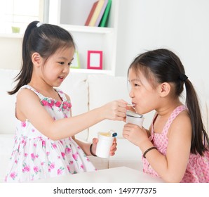 Eating yogurt. Happy Asian children eating yoghurt at home. Beautiful sisters . Healthcare concept.