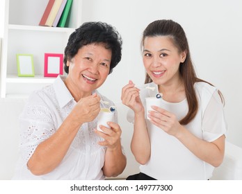 Eating Yogurt. Happy Asian Family Eating Yoghurt At Home. Beautiful Senior Mother And Adult Daughter, Healthcare Concept.