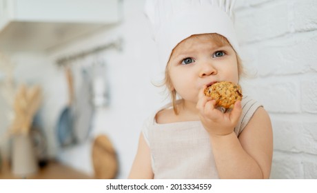 Eats cookies for breakfast. The little chef enjoys the taste of food. The child plays exciting games at home. A girl of European appearance.