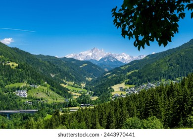Eben im Pongau, Salzburg - Austria - 06-16-2021: Scenic view from hilltop of alpine village nestled in green valley with snow-capped mountain in background - Powered by Shutterstock