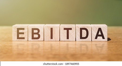 EBITDA (abbreviation of earnings before interest, taxes, depreciation and amortization) word written on wooden blocks on wooden table. Concept for your design.