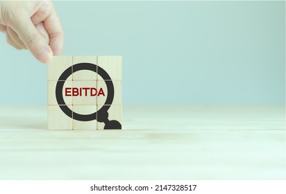 EBITDA Earnings Before Interest, Taxes, Depreciation and Amortization.Business, financial, money investment profit concept. Hand placed wooden cubes with "EBITDA" text and magnifier glass icon.