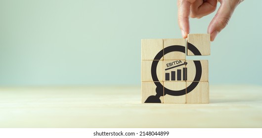 EBITDA Earnings Before Interest, Taxes, Depreciation and Amortization. Business, financial, money investment profit concept. Hand placed wooden cube with focused"EBITDA" text and increasing graph.
