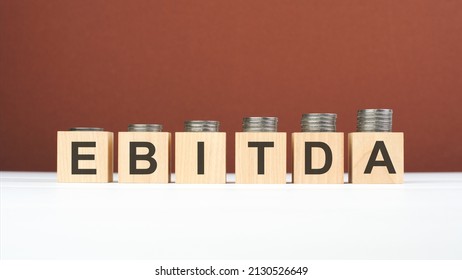 EBITDA text on wooden blocks with coins on brown background, business concept. EBITDA - short for earning before interest taxes depreciation and amortization - Shutterstock ID 2130526649