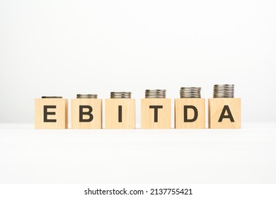 EBITDA text written on wooden block with stacked coins on white background, growing trend, business concept. ebitda - short for earning before interest taxes depreciation and amortization