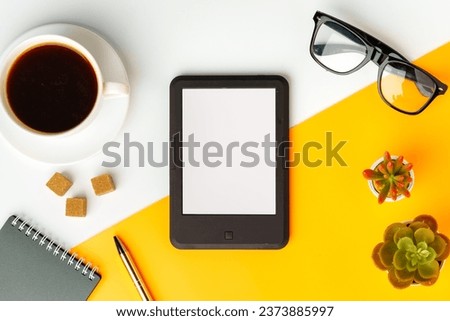 E-book reader with coffee cup and glasses on white and yellow background