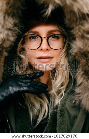 Eccentric female in glasses and hat portrait. Funny young beautiful girl fooling . Beautiful artistic model in jacket with faux fur making funny faces. Old fashioned style aristocrat bizarre woman