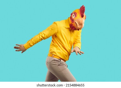 Eccentric Man In Funny Rubber Chicken Head Mask Isolated On Blue Studio Background Dancing. Cool Guy In Headwear Have Fun Make Dancer Moves. Carnival Or Masquerade, Entertainment.