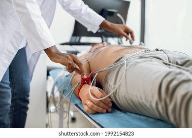 ECG Electrocardiography And Regular Health Check Concept. Electrocardiogram For Heart And Pulse Measurement In Clinic. Female Afro Nurse Sticking Vacuum Electrodes On Patient Chest
