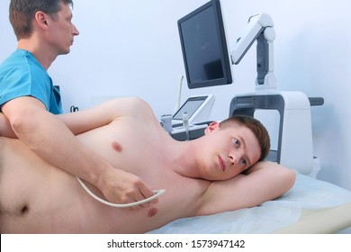 Echocardiography. Man doctor examining guy patient's heart by using ultrasound equipment. He runs ultrasound sensor over man's chest on heart area, working on scanner panel, looking at screen.
