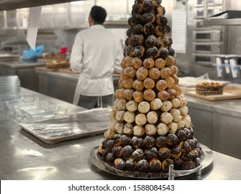 Eclair Pyramid Is On The Table In The Galley Of The Cruise Ship. Chef On A Background Is Cooking A Dessert.