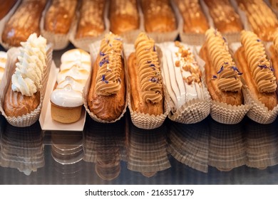 Eclairs on the shelf of a pastry shop or cafe. Tasty french sweets on window shop, delicious pastries for coffee. Cakes in pastry shop, variety of desserts with creamy topping on display in bakery.