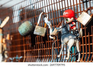 Eclectic collection of objects attached to a rusty metal fence, including pieces of plastic, toys, string and other colorful found items.