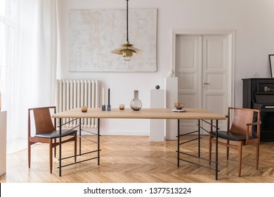 Eclectic and elegant dining room interior with design sharing table, chairs, gold pendant lamp, abstract paintings, piano and stylish accessories. Minimalistic decor. Brown wooden parquet. Real photo.