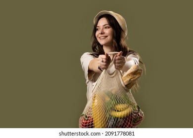 Eco bag string bag with fruits, vegetables, juice and bread in a hands of a brunette girl in a beige suit and a hat. Eco friendly concept. Fashion photography. Zero waste concept.