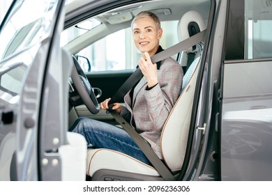 Eco Car Sale, Portrait Of Smiling Young Caucasian Woman Sitting Alone On Driver Seat Of Electric Car With Fasten Belt While Driving Modern Car. Lifestyle And Success Concept.