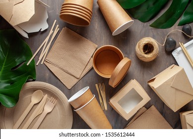 Eco craft paper tableware. Paper cups, dishes, bag, fast food containers and wooden cutlery on wooden background. Recycling or eco-friendly concept. Top view. 