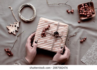 Eco Friendly Decorations - Recycled Craft Wrapping Paper, Hawthorn Berry, Wattle Wreath, Wooden Christmas Toys. Hands Wrapping Xmas Gift Box With Natural Christmas Decor On Natural Beige Textile.